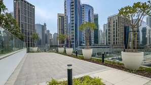 Una terraza en la azotea con plantas en macetas, barandilla de vidrio y vistas a modernos edificios altos.