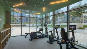 Un gimnasio moderno con equipo de ejercicio, ventanas amplias y vistas a la ciudad.