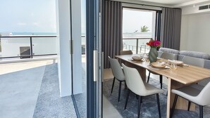 A modern dining area with a table set for four, a sofa, and a view of the sea. - The Village Chumphon Hotel (Pathio)