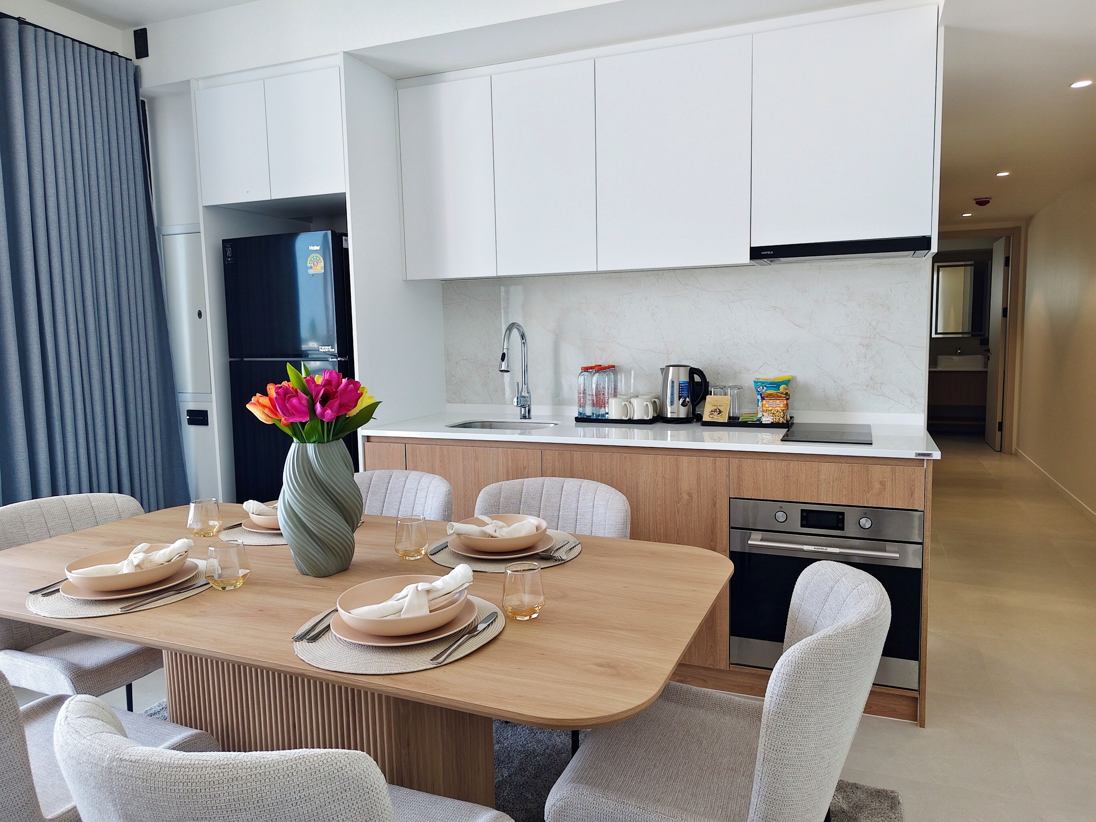 A modern kitchen with white cabinets, a built-in oven, and a dining area with a wooden table set for four.