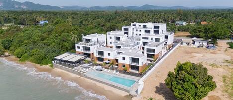 A modern hotel with a pool, located near a beach and surrounded by greenery.