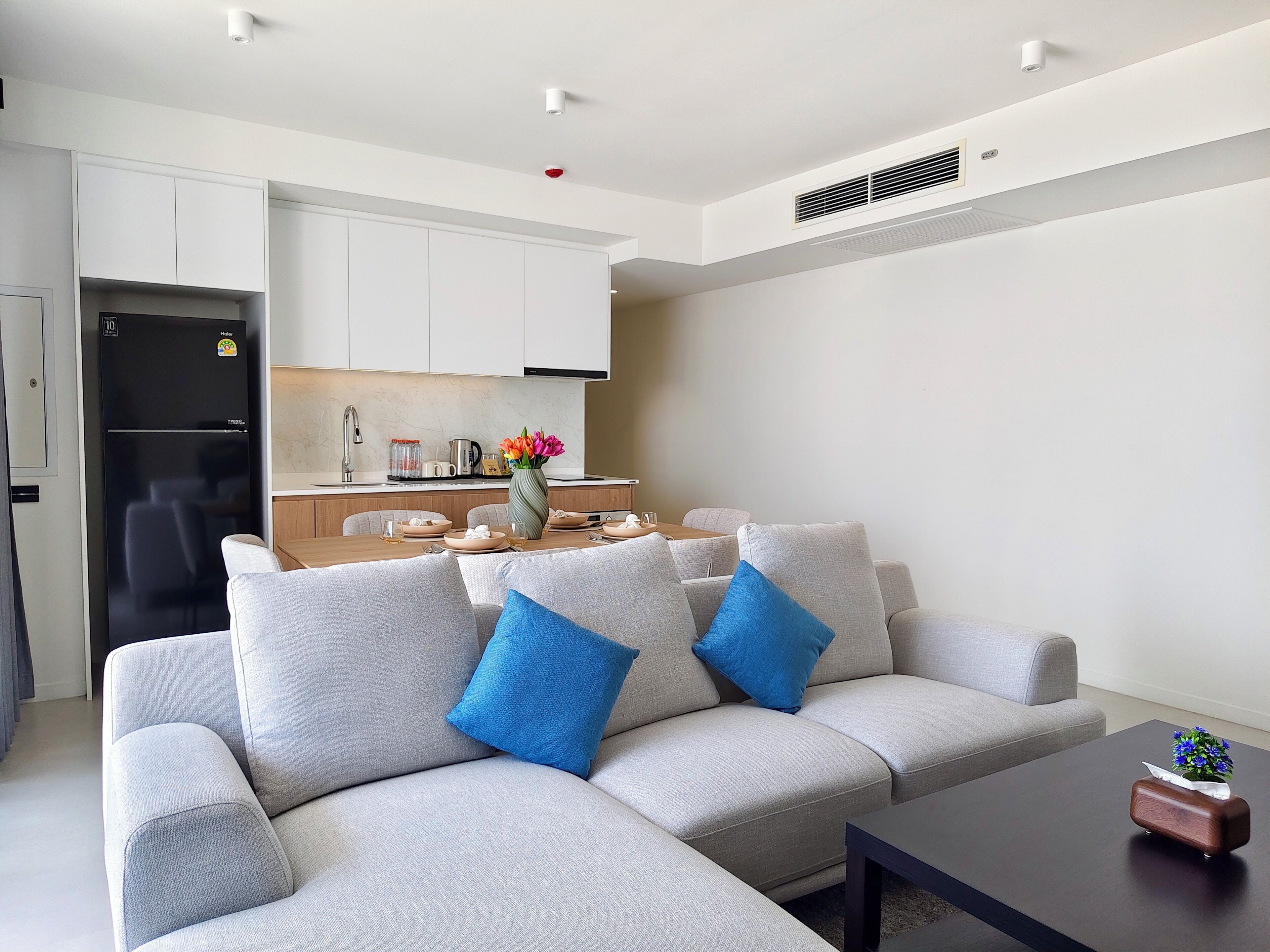 Una sala de estar moderna con un sofá, una mesa de centro y una pequeña cocina al fondo.