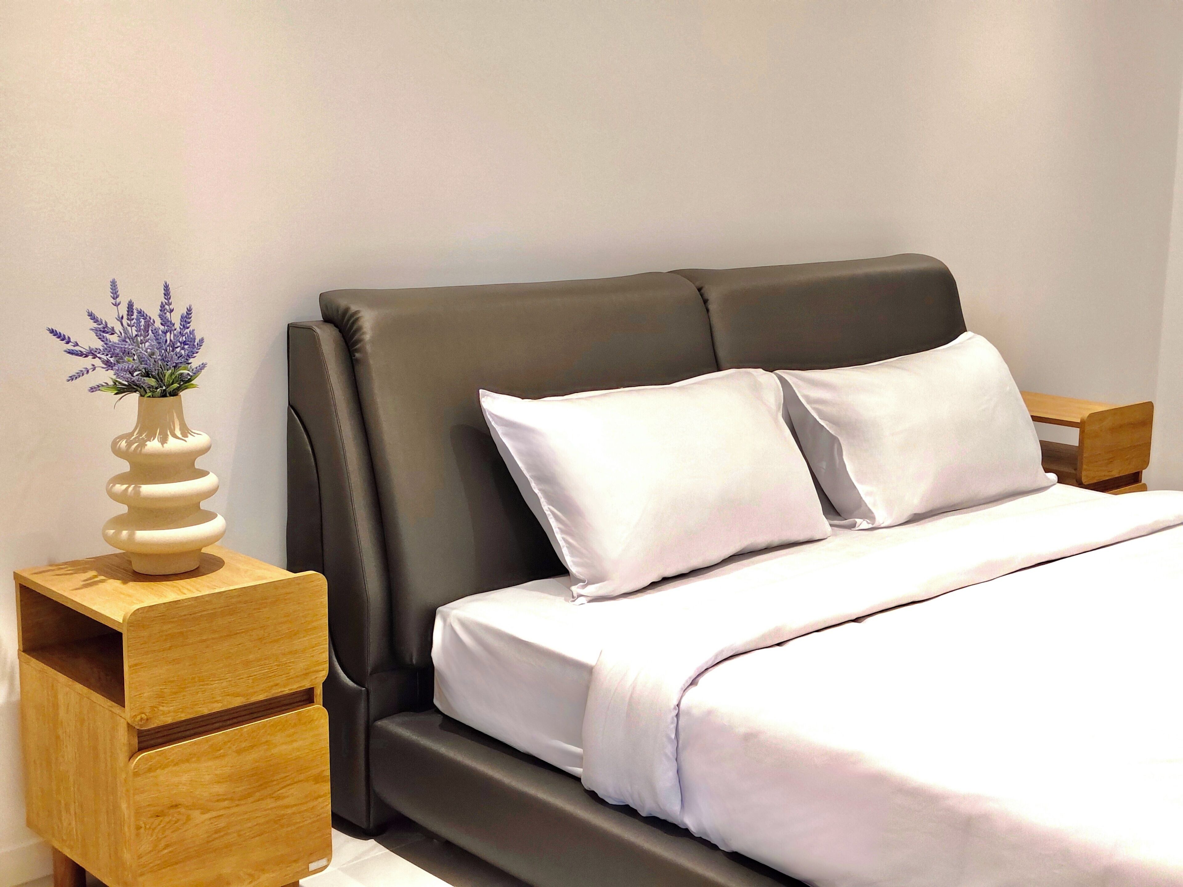 A modern bedroom with a bed, two pillows, a nightstand, a wooden side table, and a vase with flowers.