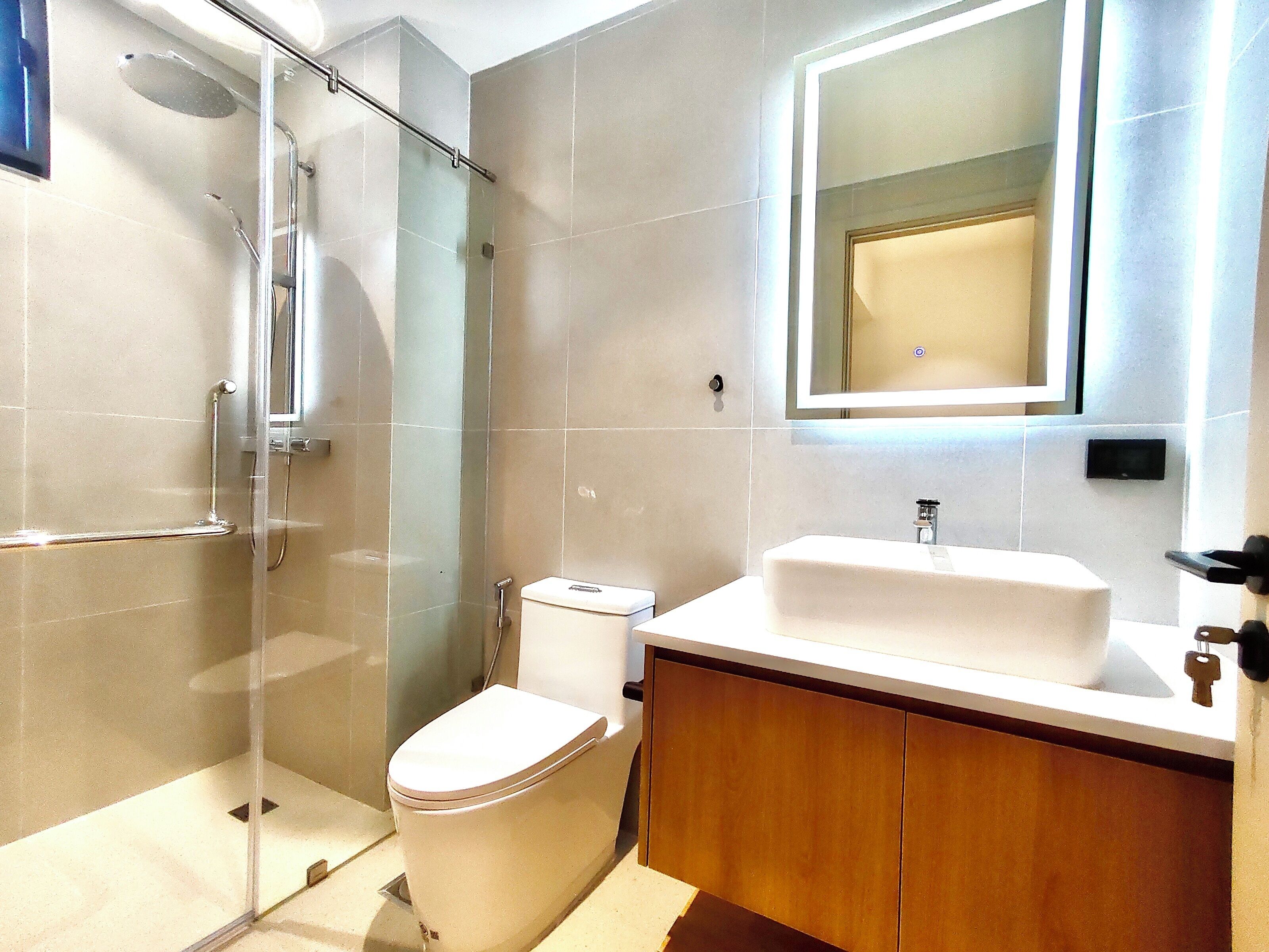 Un baño moderno con cabina de ducha de vidrio, inodoro y tocador con lavamanos.