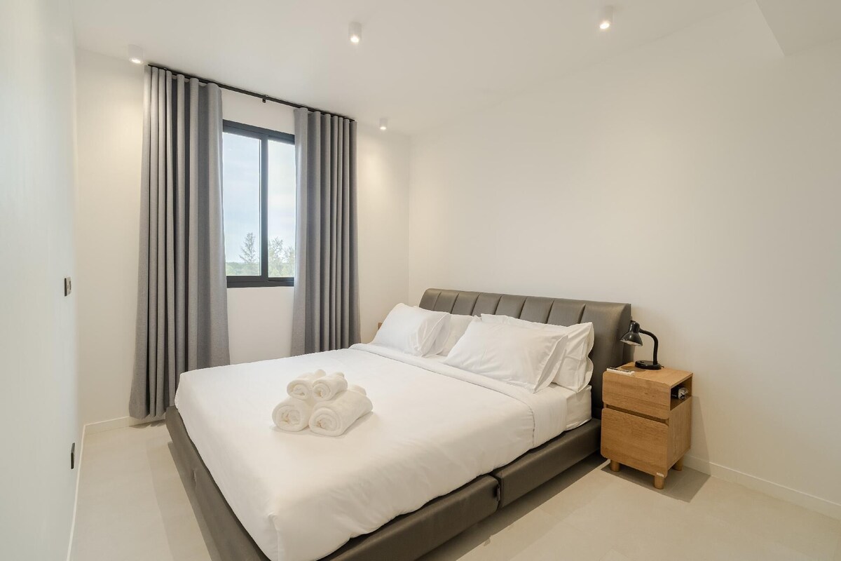 Una habitación de hotel moderna con una cama grande, una mesita de noche y una ventana con cortinas.