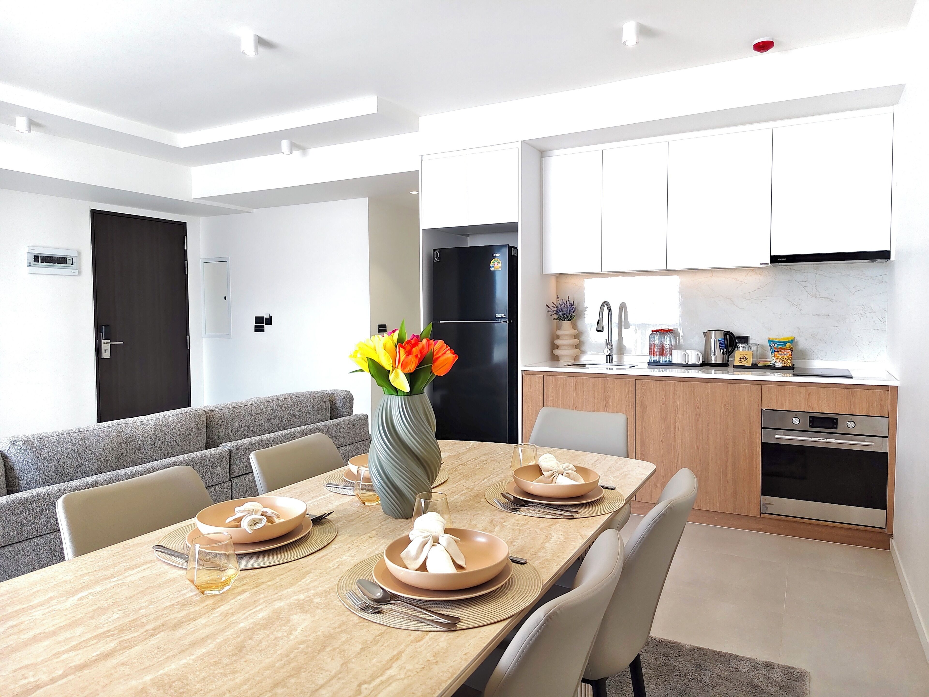 Una cocina moderna con armarios blancos, un refrigerador negro y un comedor con una mesa de madera dispuesta para cuatro.