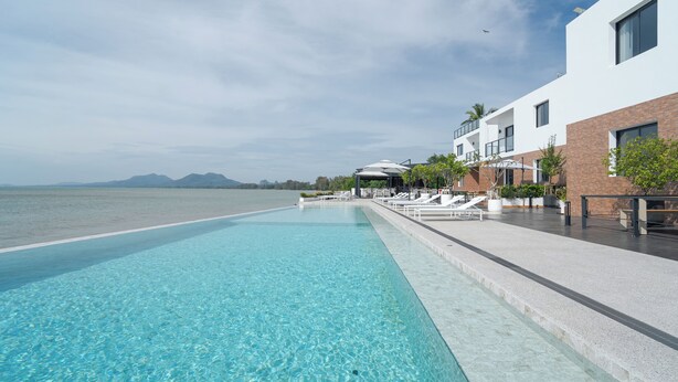 A clear swimming pool with lounge chairs and a building adjacent to it. - The Village Chumphon Hotel (Pathio)
