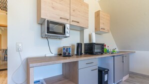 A kitchenette with a microwave, toaster, and coffee maker on the counter, a trash bin, and wooden cabinets. - Pferdehof Königsstuhl - Apartment 1 Mecklenburger - Holidays at the riding stable - (Lohme)