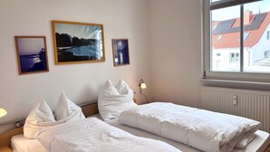 Una habitación con dos camas, una mesita de noche, una lámpara y tres cuadros en la pared.