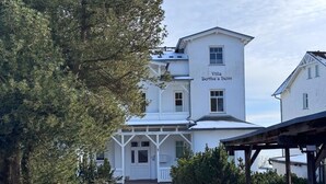 Un edificio blanco con un letrero que dice 'Villa Bertha's heim' y un sendero de ladrillo que conduce a la entrada.
