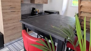 A modern kitchen with wooden cabinets, a black countertop, and red chairs. - ROOM FOR RENT IN A GUEST HOUSE (Navarrenx)