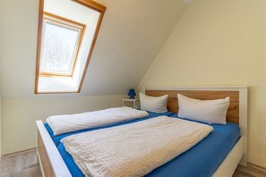 Ein Schlafzimmer mit zwei Betten, einem Oberlicht, einem Nachttisch mit Lampe und einem Holz-Kopfteil.