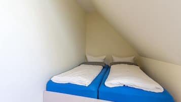 Une petite pièce unique comprenant deux lits, un plafond en pente et des murs sobres.