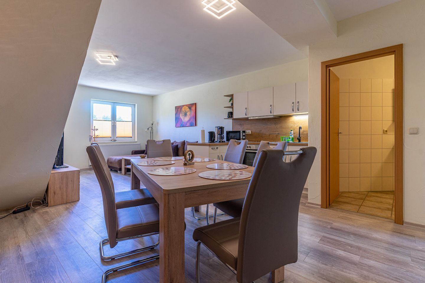 Un espace repas avec une table en bois, des chaises et une cuisine en arrière-plan.