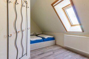 Een kleine zolderkamer met een schuine plafond, een dakraam, een radiator en een bed met blauw beddengoed.