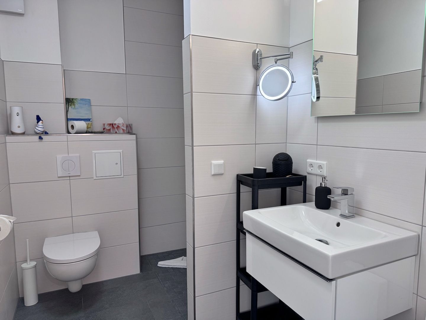 A modern bathroom with a toilet, sink, and a mirror with a circular light.