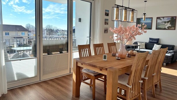 Ein Essbereich mit einem Holztisch und Stühlen, einer Vase mit rosa Blumen und Blick durch große Schiebeglastüren.