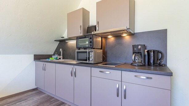 Una kitchenette compacta con microondas, cafetera y armarios.
