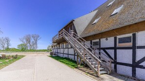 Een gebouw met een trap naar een deur, een geplaveid pad en een omheind gebied met bankjes.