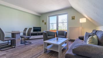 A modern living room with a TV, seating, and a large window.
