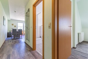 Un pasillo con una puerta de madera, un comedor con sillas y vista a un baño.