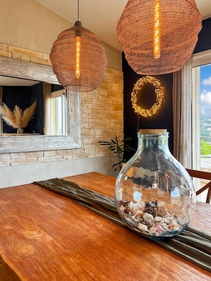 A dining area with a wooden table, two woven pendant lights, a glass vase with seashells, a mirror, and a stone wall. - Large charming villa Porto-Vecchio swimming pool/poolhouse in private grounds (Porto-Vecchio)
