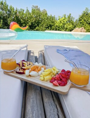 A poolside table with a fruit platter and two glasses of orange juice. - Large charming villa Porto-Vecchio swimming pool/poolhouse in private grounds (Porto-Vecchio)