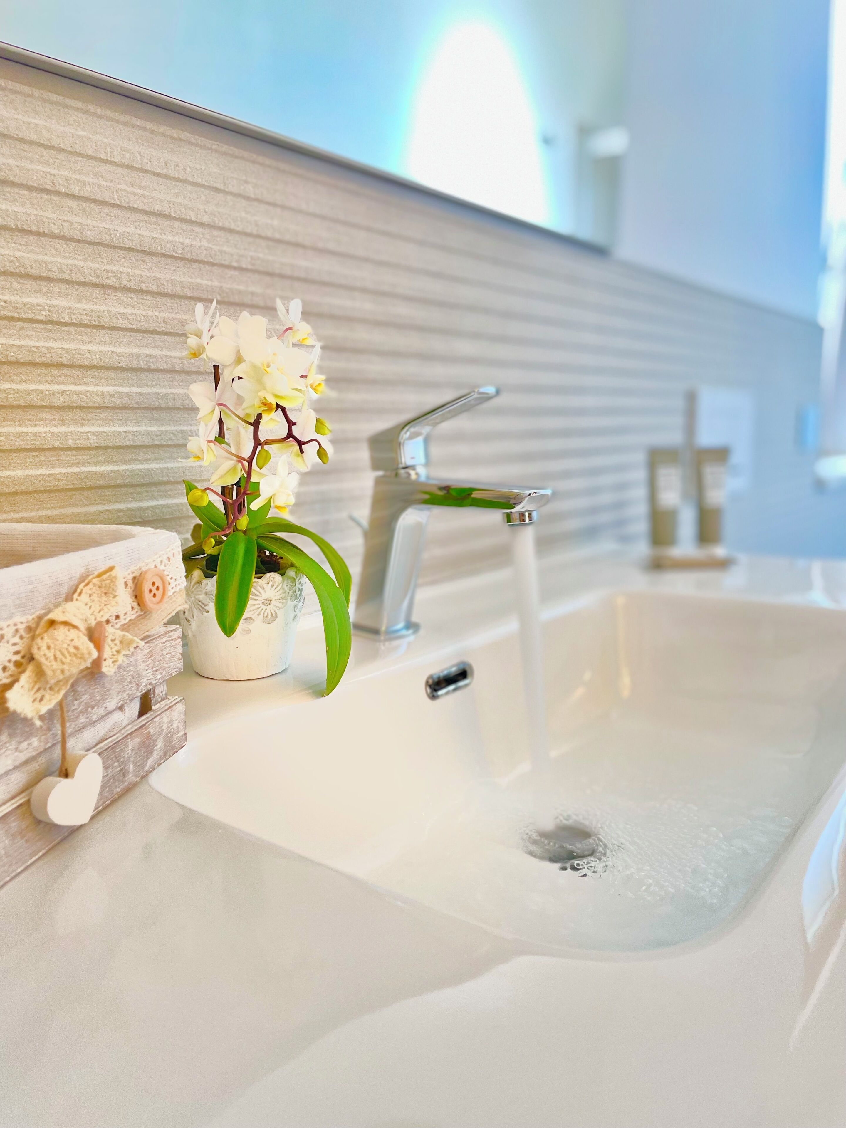 A bathroom with a white sink, a modern faucet, a potted orchid, and a decorative heart ornament.