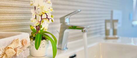 A bathroom with a white sink, a modern faucet, a potted orchid, and a decorative heart ornament.