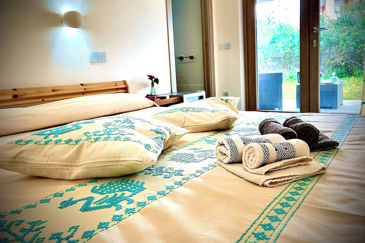 A bedroom with a bed, pillows, a bedside table, and a view through a glass door.