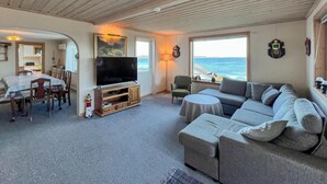 Een woonkamer met een televisie, een bank, een eettafel en uitzicht op zee.