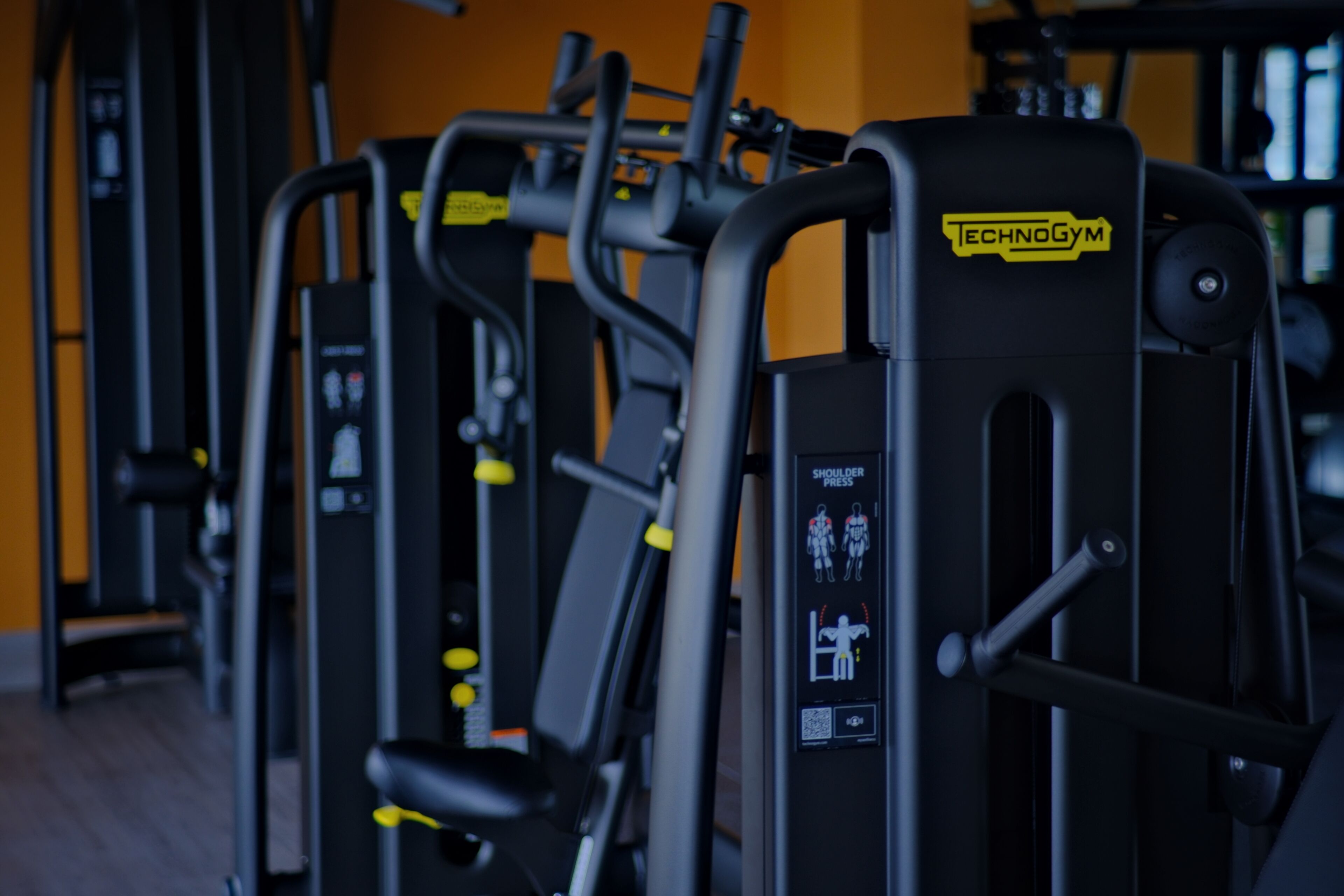 A row of gym equipment with a sign indicating shoulder press.
