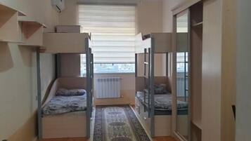 A narrow room with bunk beds, a radiator, a window with blinds, and a patterned rug.