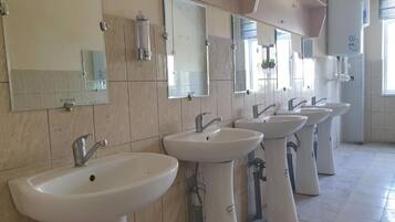 A row of sinks and mirrors in a restroom with tiled walls and a window.