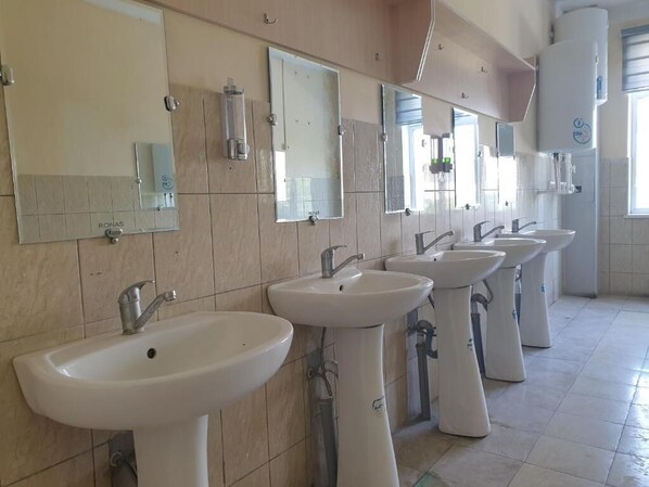 Une rangée d’éviers et de miroirs dans des toilettes dont les murs sont recouverts de carreaux et qui comportent une fenêtre.