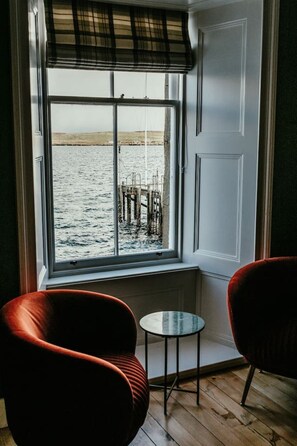 A room with a large window overlooking a body of water, a small table, and two chairs. - NEW to VRBO: Luxury Seafront Stay in Central Lerwick W/ Parking (Lerwick)