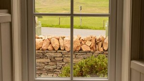 A window with a stone wall and a grassy landscape outside.