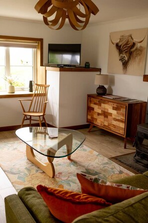 Een woonkamer met een tafel met glazen blad, een houten stoel, een bank, een televisie en een decoratief schilderij van een stierenhoofd.