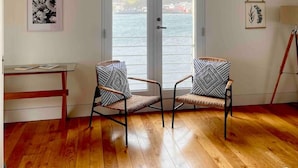 Una habitación con suelo de madera, dos sillones estampados, una mesa y vistas a través de una puerta.