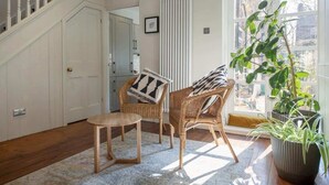 Una habitación con una escalera, sillas de mimbre, una mesa redonda, un radiador y un ventanal con vistas.