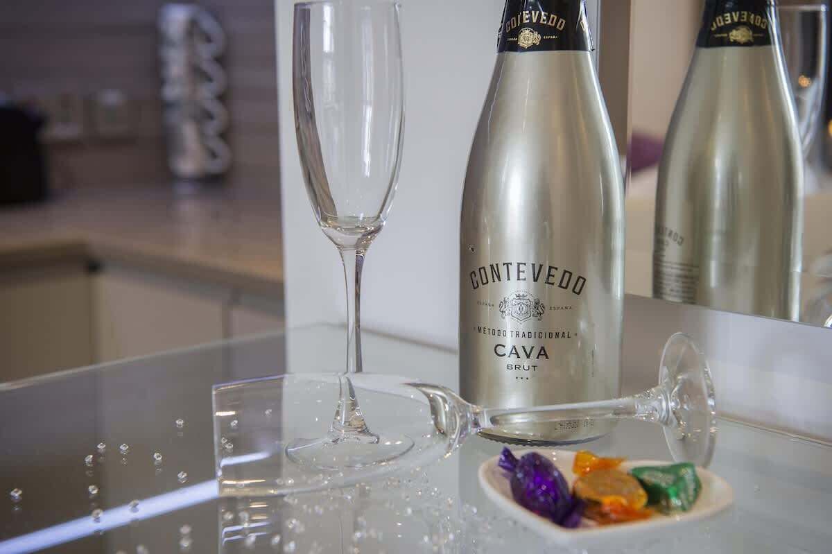 A bottle of Conteveddo Cava Brut wine, a glass, and a teapot on a reflective surface.