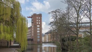 Un canale con un edificio in mattoni, un salice piangente e un albero.