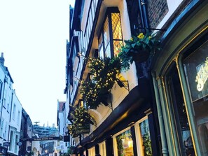 Uma rua estreita com edifícios com grandes janelas e vasos de flores pendurados.