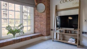 A room with a large window, a brick fireplace, a television on a wooden stand, and a wall sign that reads 'The Cocoa Suites.' - The Cacao Suite - Charming River View Apartment Steps from York City Centre (York)