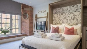 A hotel room with a bed, a brick wall, a large window, and a sign that reads 'The Cocoa'. - The Cacao Suite - Charming River View Apartment Steps from York City Centre (York)