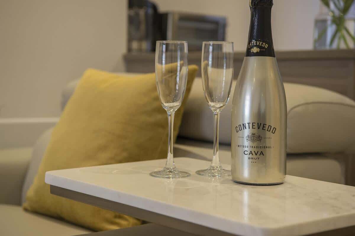 A bottle of Cava wine and two glasses on a white table in a living room.