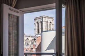 Uitzicht vanuit een raam op een historisch gebouw met gotische architectuur, herkenbaar aan puntbogen en een hoge toren.