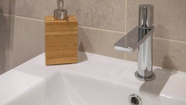 Un lavabo de salle de bain doté d’un robinet moderne et d’un distributeur de savon en bois.