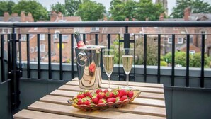 Un balcon avec une table dressée pour deux personnes, agrémentée d’une carafe, de deux verres et d’un saladier rempli de fraises.