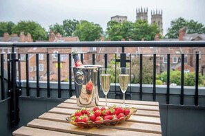 A balcony with a table set for two, featuring a pitcher, two glasses, and a bowl of strawberries. - The Carillon Suite - Stylish Duplex w/ York Minster Views & Free Parking (York)
